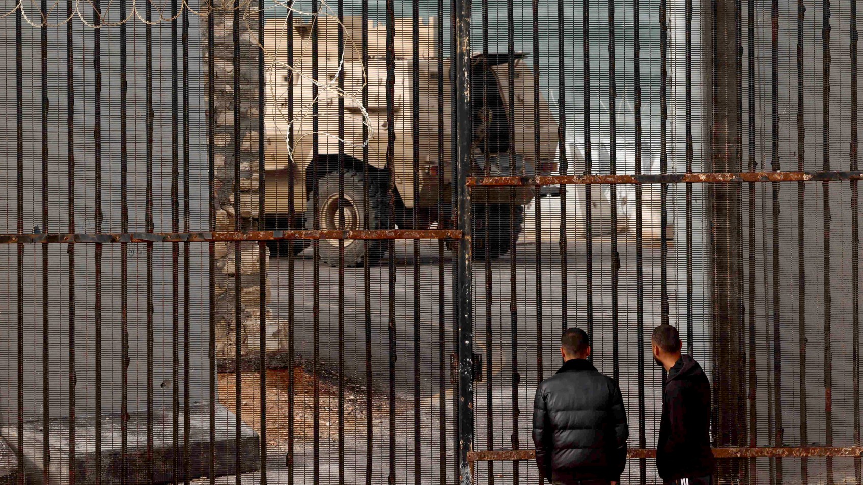 Displaced Palestinian men watch as an Egyptian army armoured personnel carrier drives near border fence between Gaza and Egypt, on February 16, 2024 in Rafah
