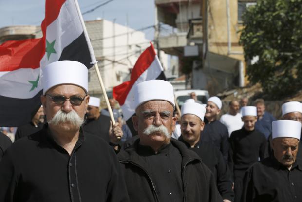 Des habitants druzes du village d’Ein Qiniye, situé sur le plateau du Golan sous occupation israélienne, brandissent des drapeaux syriens alors qu’ils manifestent lors d’un rassemblement marquant le Jour de l’indépendance de la Syrie (AFP)