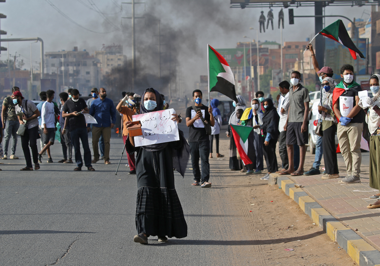 A mask-clad Sudanese woman holds a sign reading in Arabic 