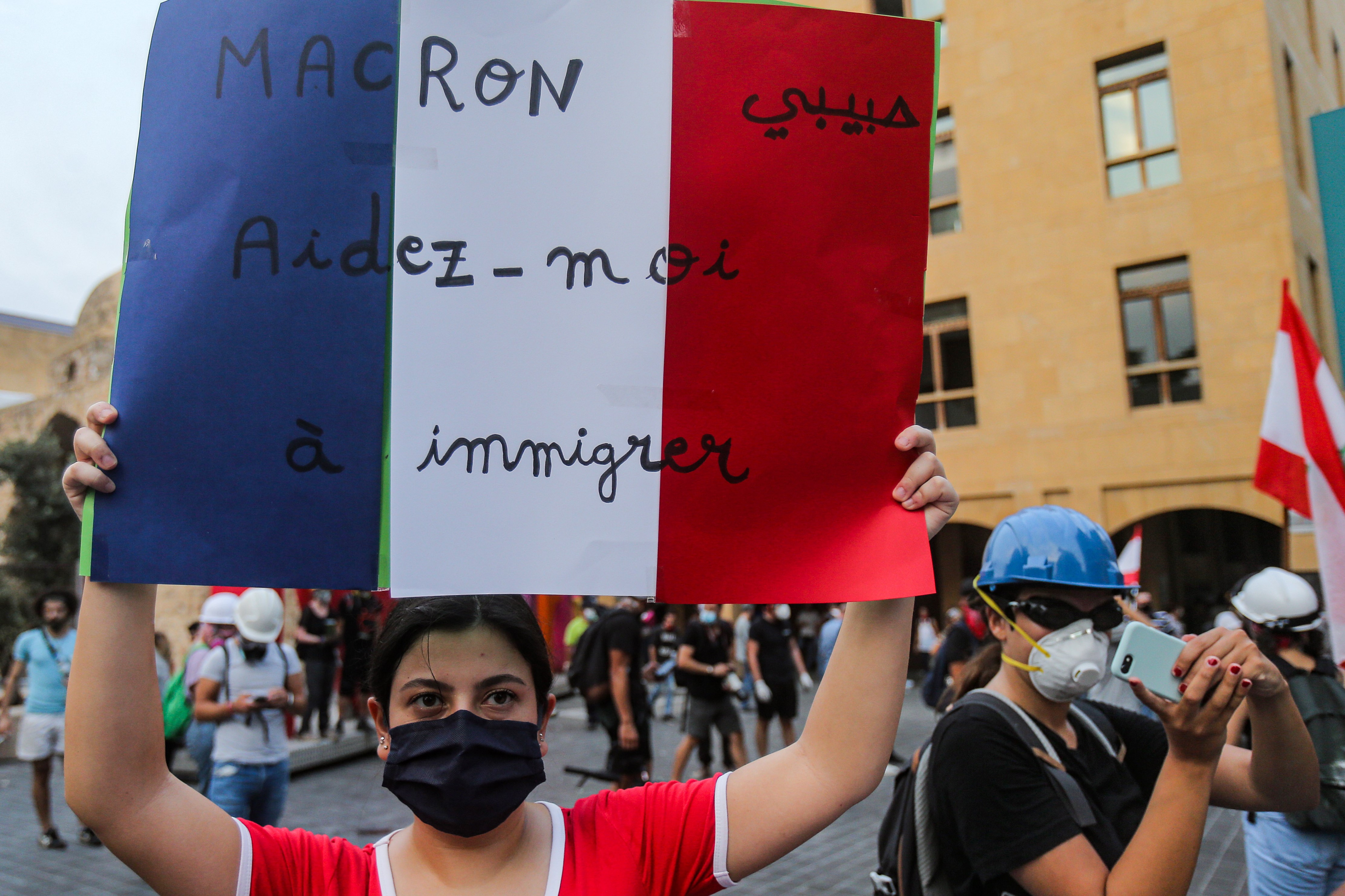 A mask-clad protester holds up a sign showing the French flag with text in Arabic and French reading 