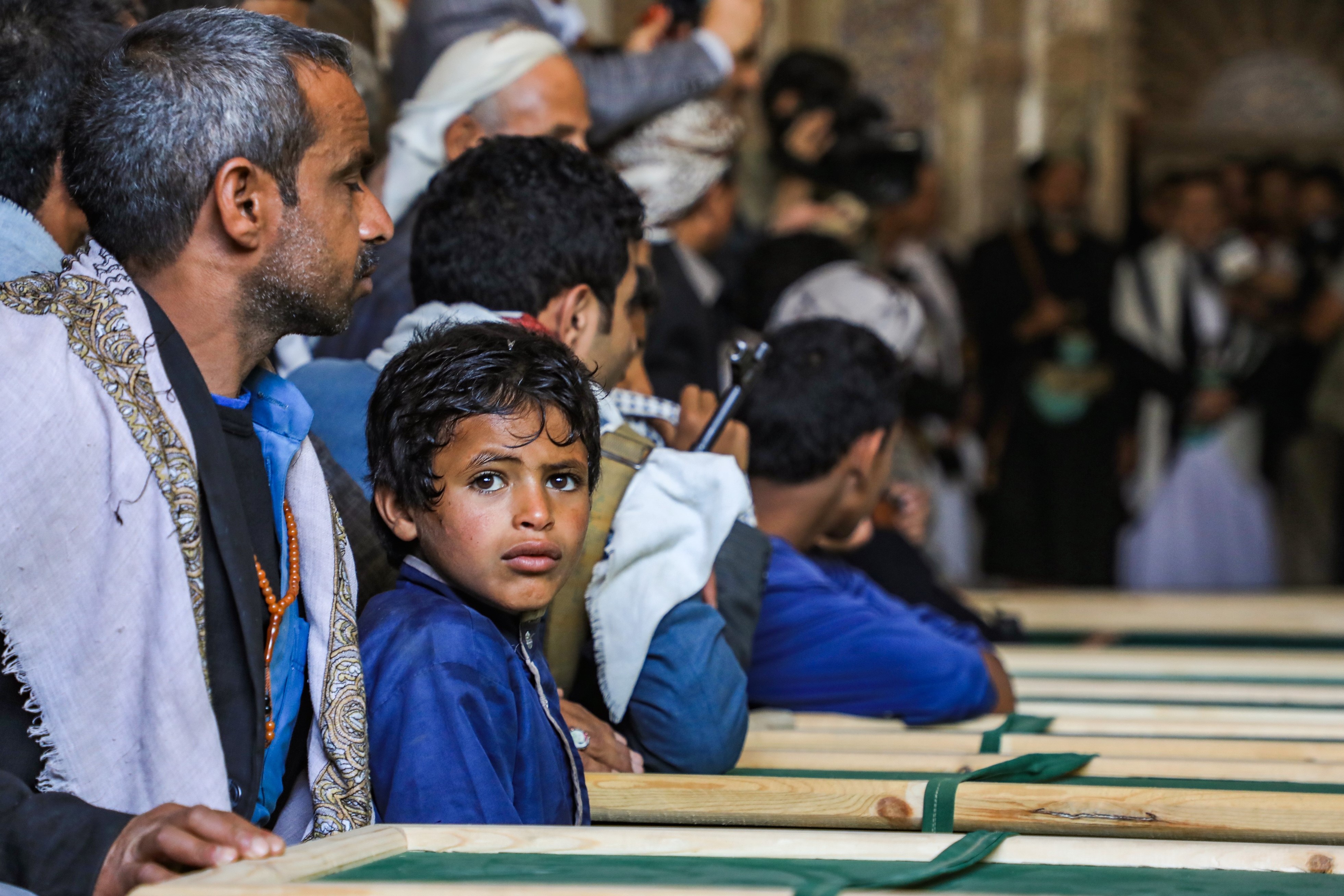 Yemeni mourners sit by coffins at a mosque during a funeral in the Huthi-rebel-held capital Sanaa on 14 March for civilians killed in strikes in the northern Hajjah province (AFP)