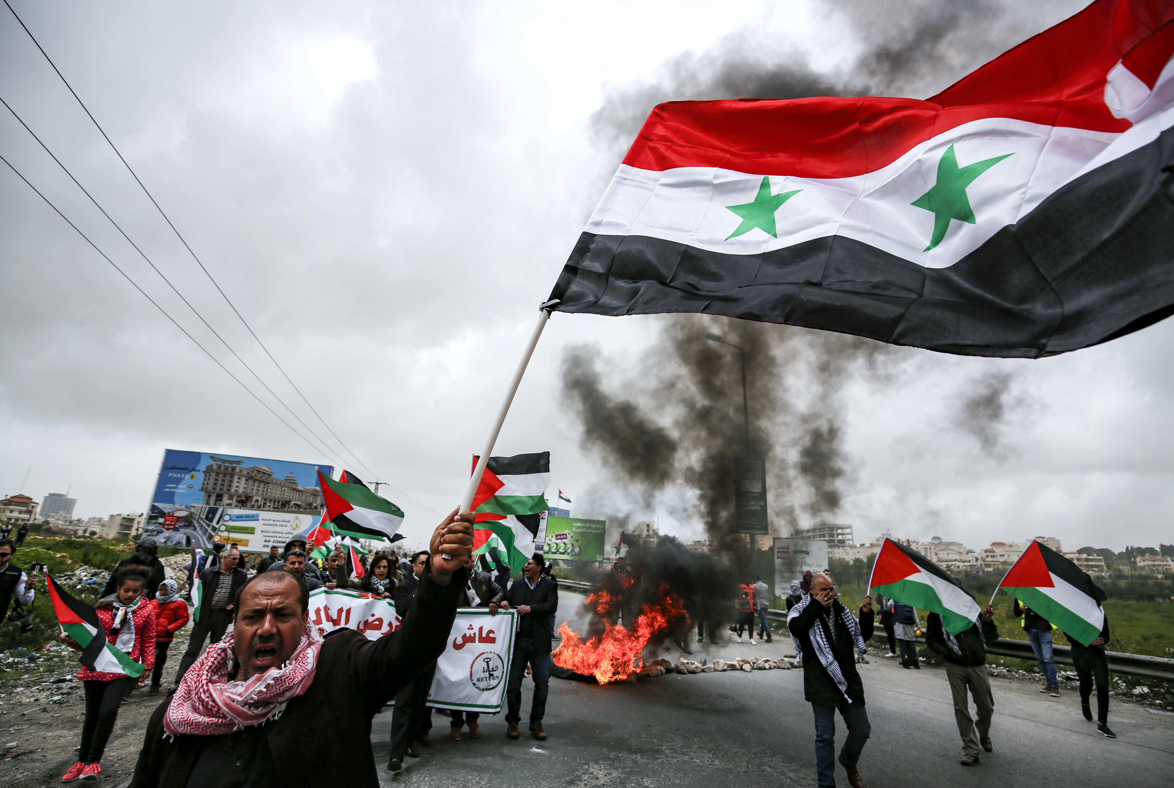 A man waves a Syrian national flag as others wave Palestinian flags behind him near the Israeli settlement of Beit El (AFP)