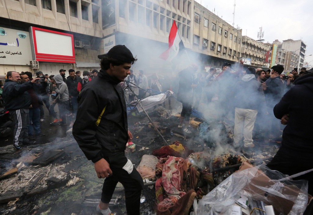 Iraqi anti-government protestors check burnt out tent after riot police cleared protest areas (AFP)