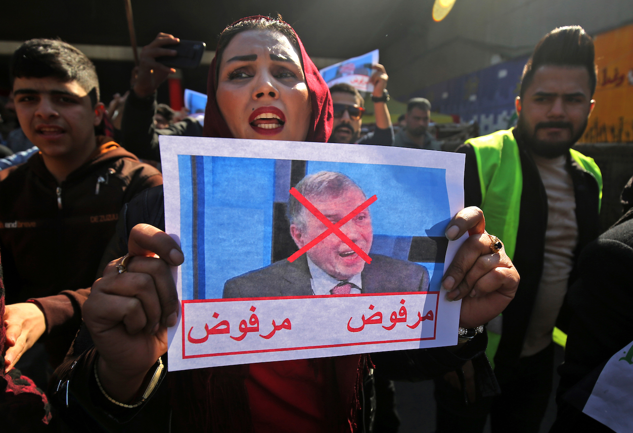 An Iraqi protester lifts pictures of the premier-designate Mohammad Allawi with the inscription 