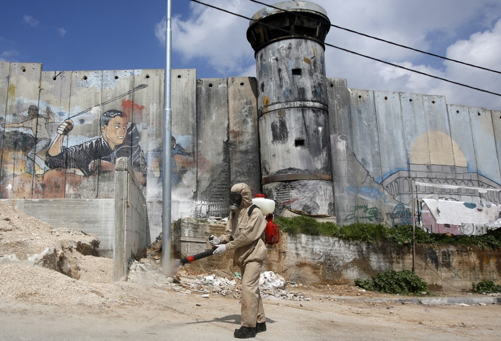 A Palestinian sanitary department worker sprays disinfectant around Aida refugee camp with Israel's separation barrier in the background (AFP)