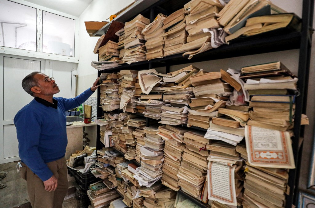 Un membre du personnel se tient devant des volumes qui nécessitent une restauration (AFP/Mahmoud Turkia)