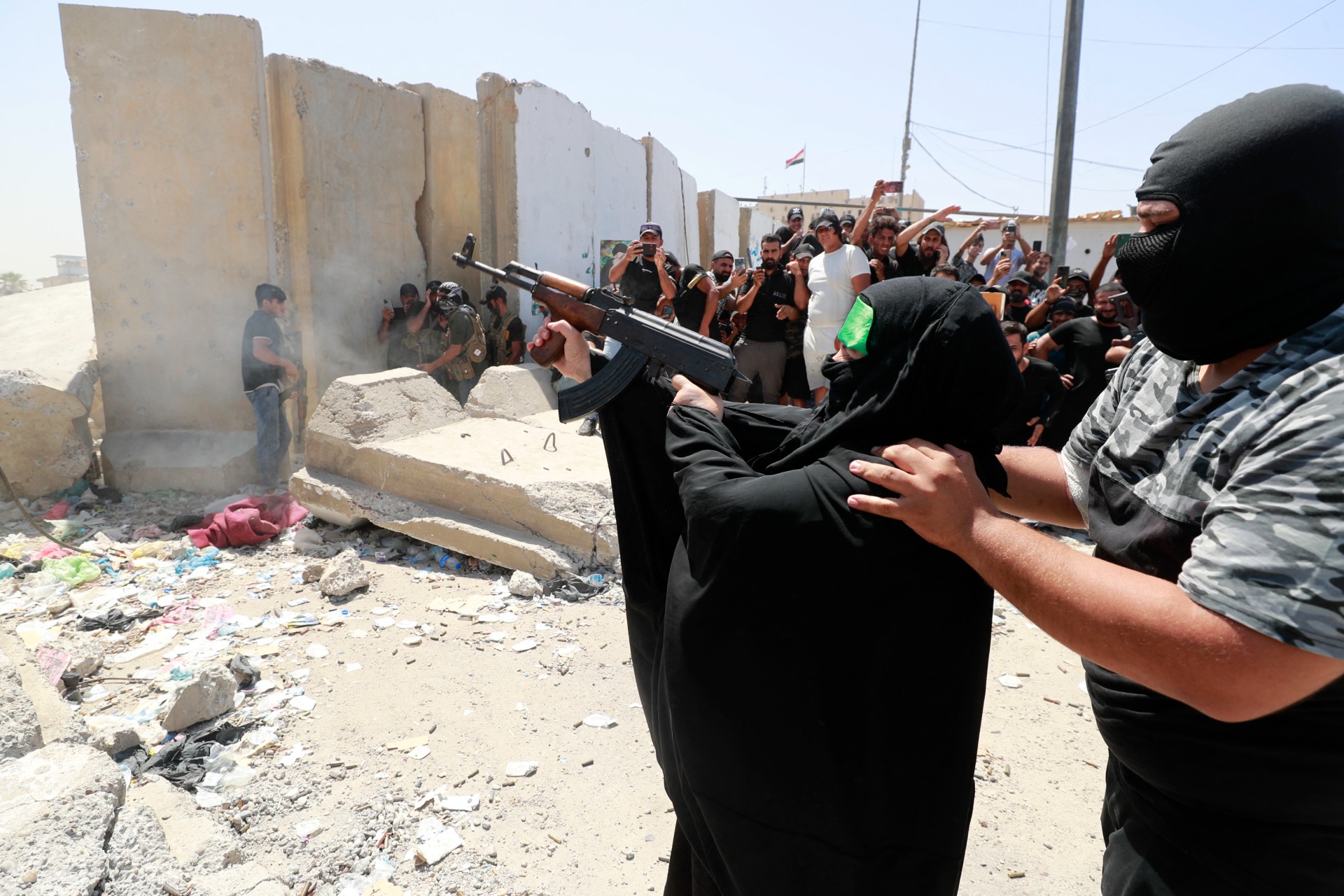A member of Saraya al-Salam helps a woman fire a gun during clashes in Baghdad, 30 August (AFP)