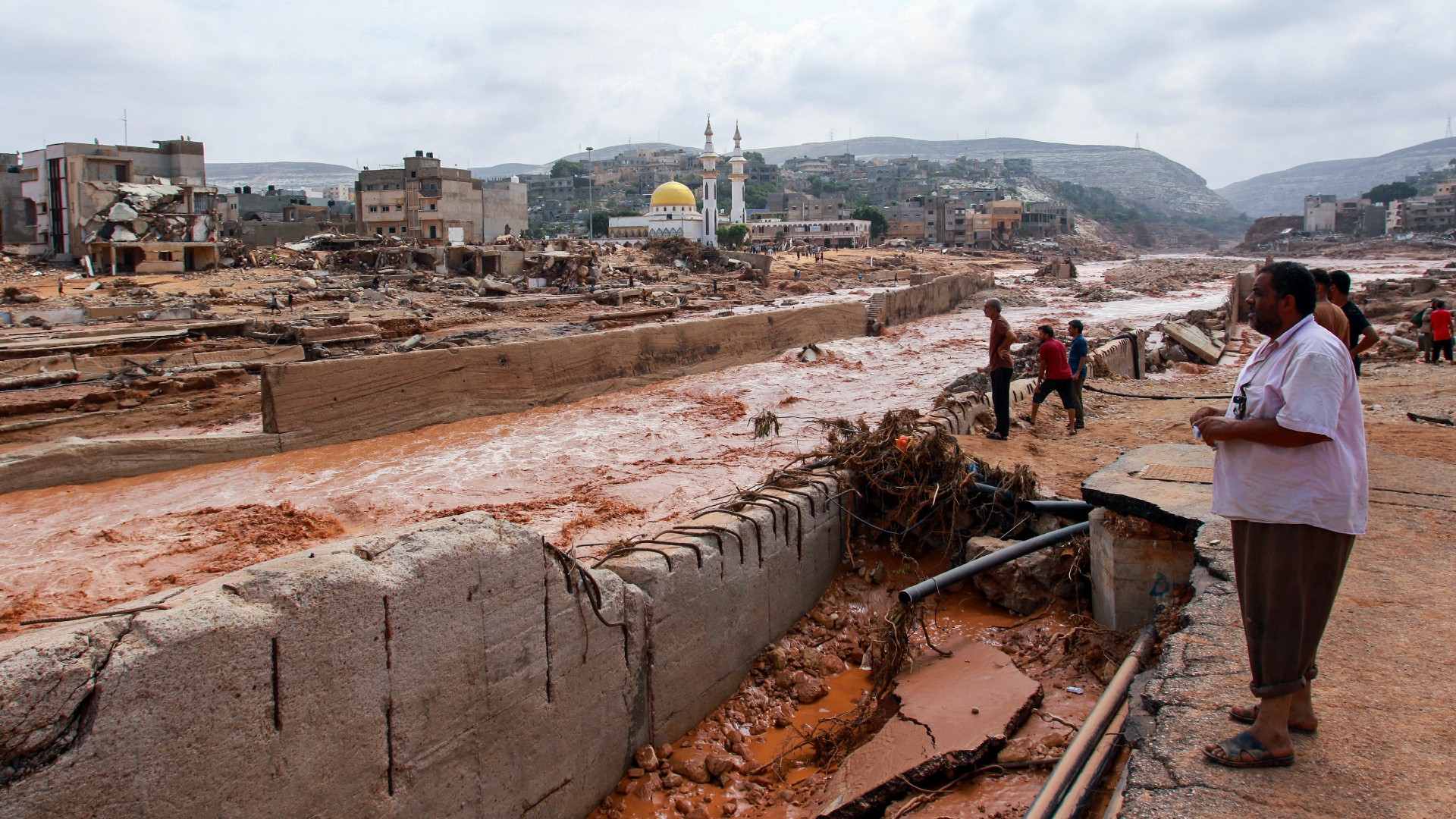 People look at the damage caused by floods in Derna alongside the canal on 11 September (AFP)