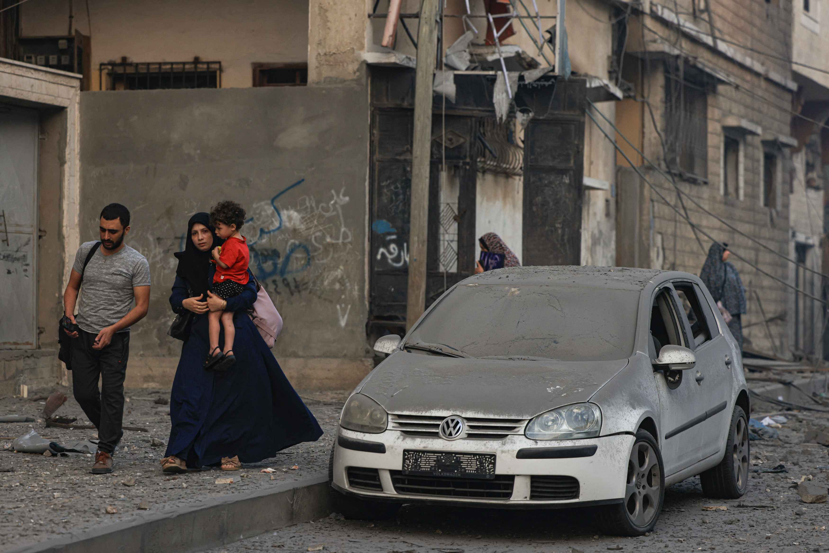 Displaced Palestinians walk along a debris-strewn street following Israeli air strikes in Gaza City early on 8 October 2023 (AFP)