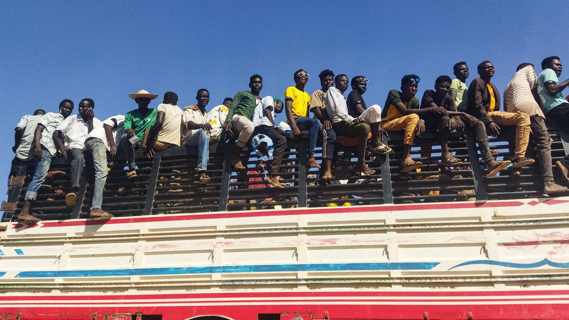 People displaced by the conflict in Sudan ride atop the back of a truck moving along a road in Wad Madani on 16 December (AFP)