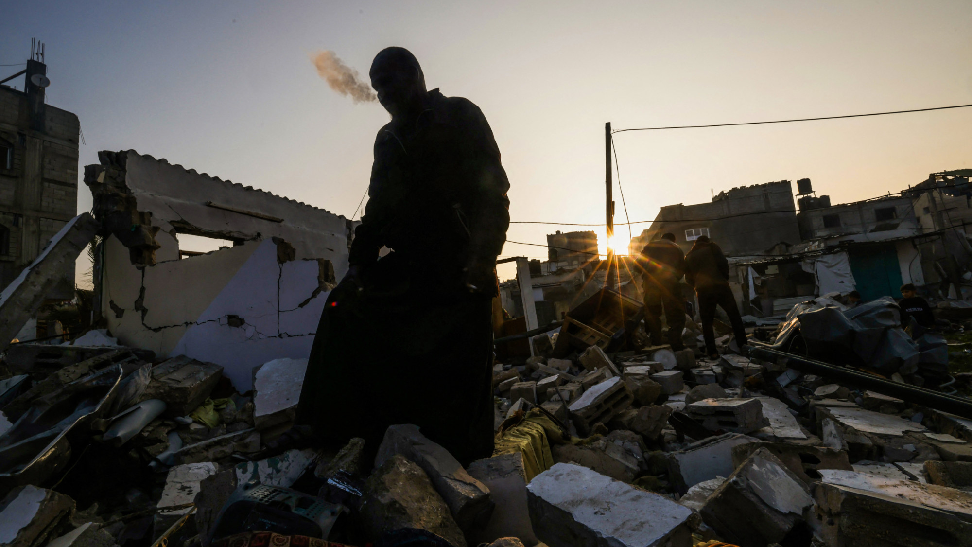 A man standing on the rubble of a building destroyed by Israeli bombardment smokes a cigarette in Rafah refugee camp, south of the Gaza Strip, on 1 January 2024 (AFP)