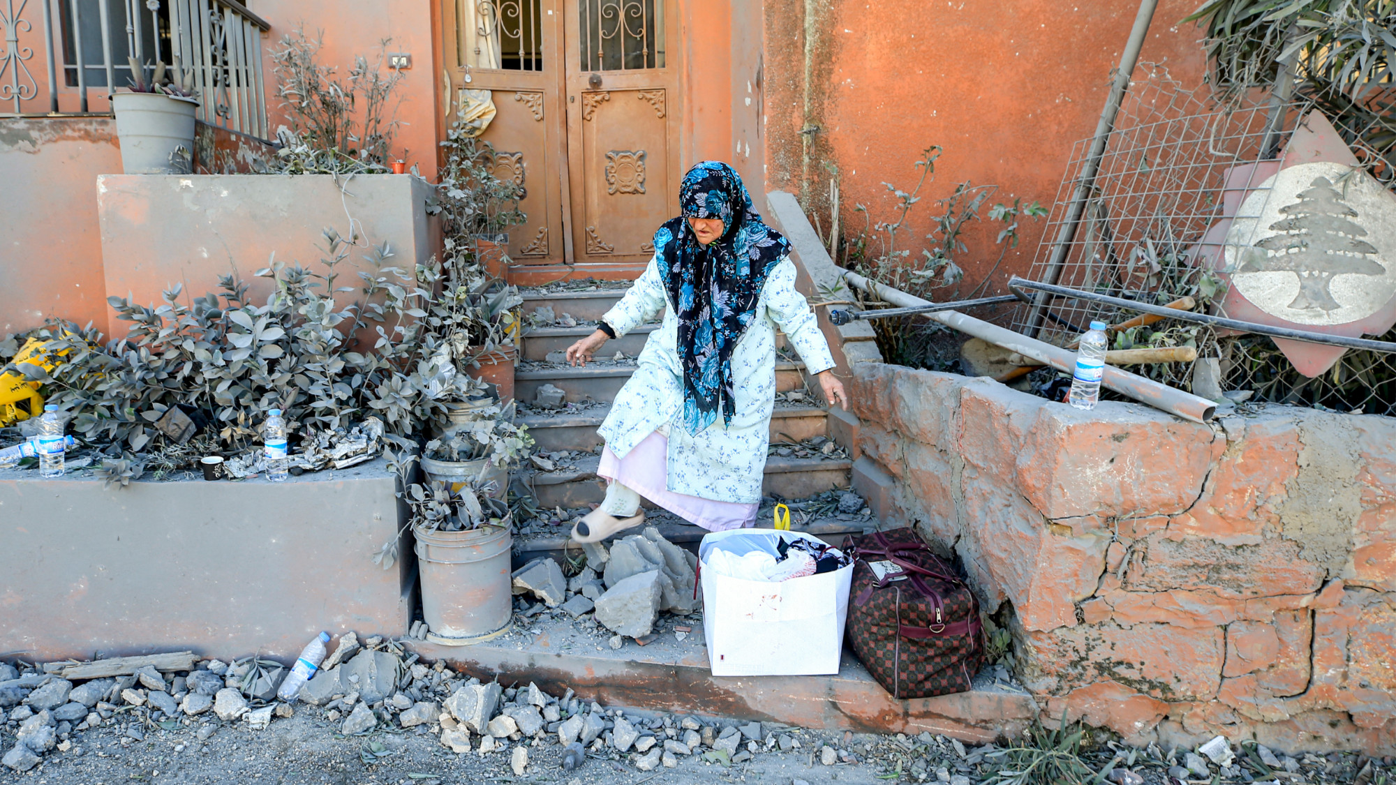 A woman walks through rubble outside a building following Israeli strikes on the the town of Naqura in southern Lebanon 4 January 2024 (AFP)