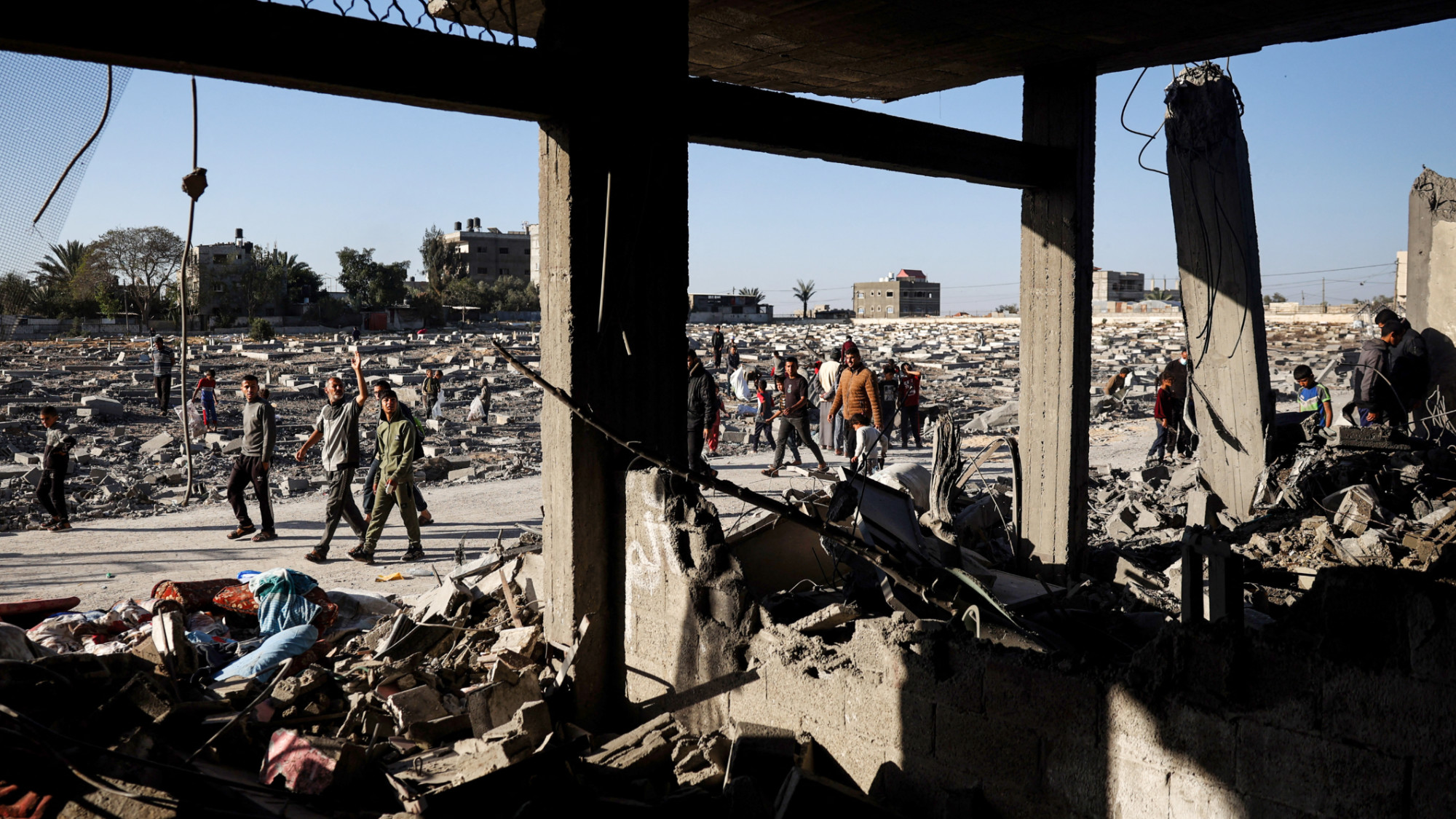 Palestinians walk between a cemetery and a building hit by overnight Israeli bombing in Rafah (AFP)