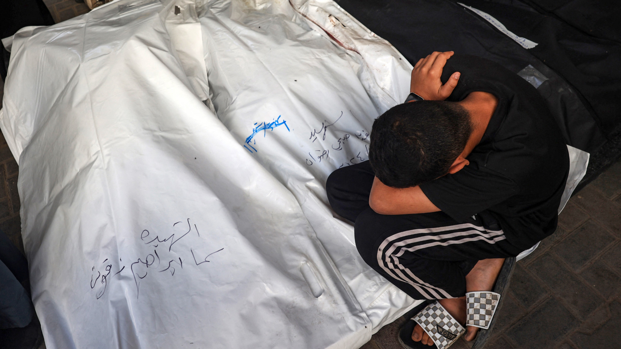 A young Palestinian boy mourns over the bodies of a children killed in Israeli bombing in Rafah in on 20 April 2024 (AFP)