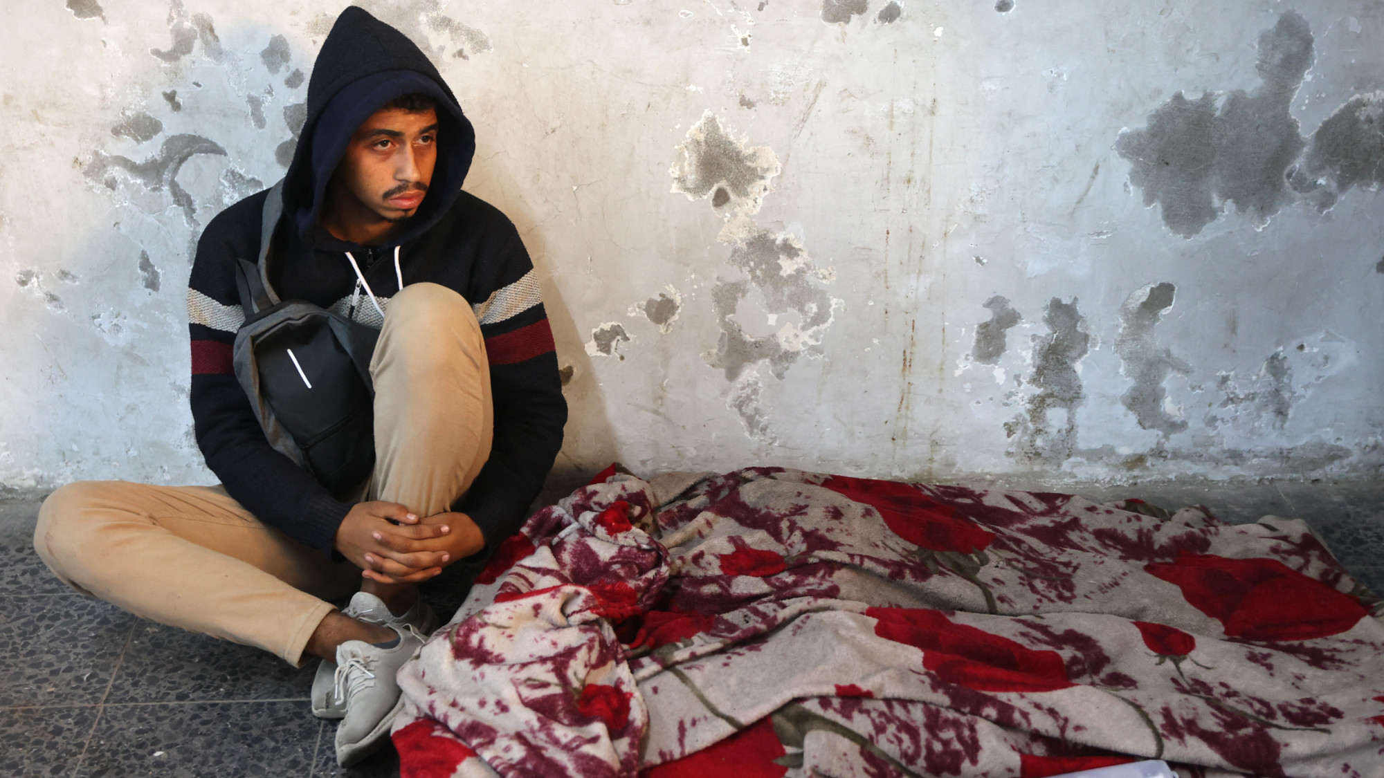 A Palestinian man mourns over the covered body of a relative, killed in an Israeli strike the previous night, at Al-Ahli Arab hospital in Gaza City on 15 December 2024 (AFP/Omar al-Qattaa)
