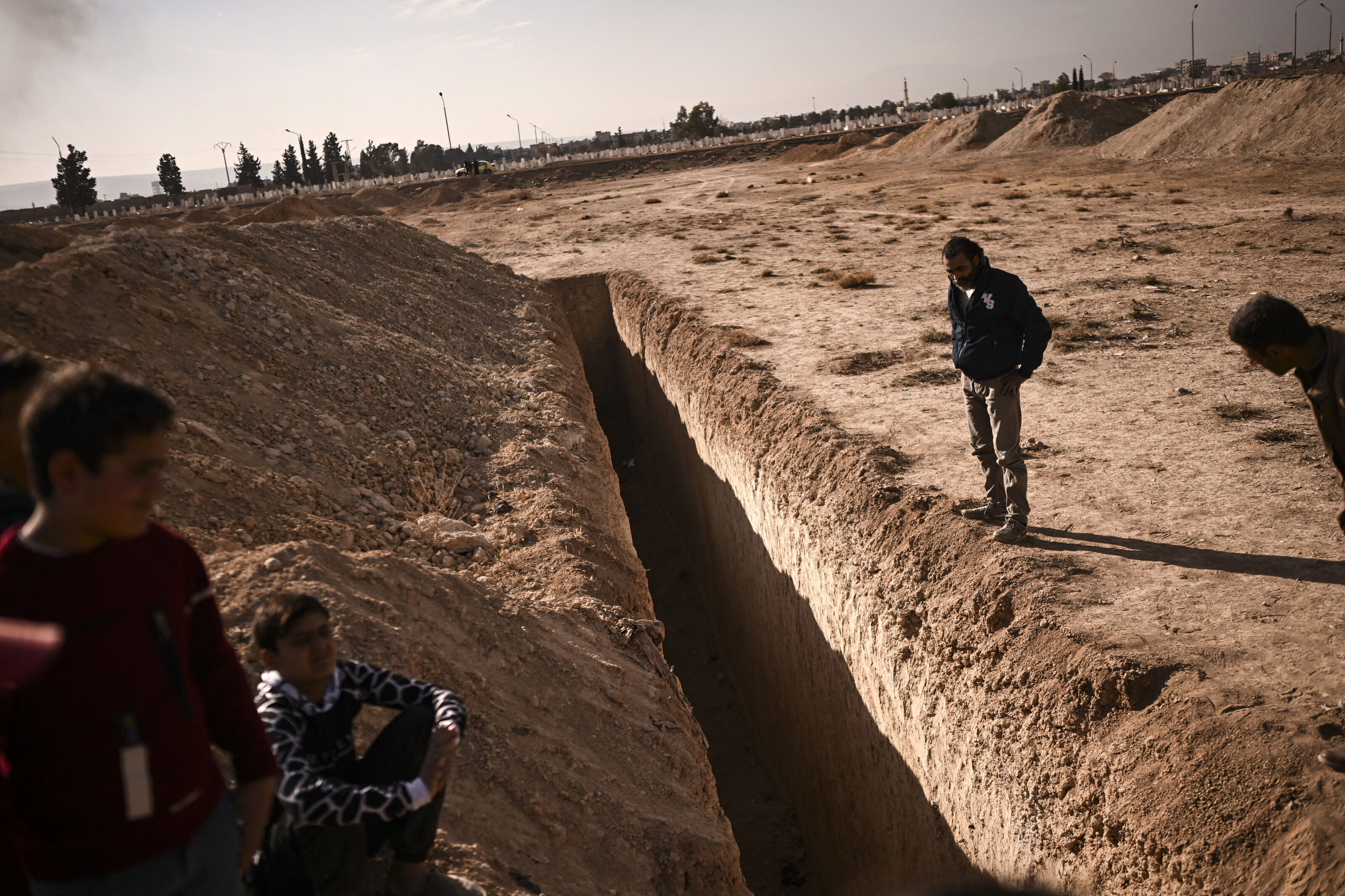 People stand next to a trench believed to be used as a mass grave on the outskirts of Damascus on December 16, 2024. Rebels took Damascus in a lightning offensive on December 8, ousting president Bashar al-Assad and ending five decades of Baath rule in Syria. According to the Syrian Observatory for Human Rights, more than 100,000 people died in Syria's jails and detention centres from 2011.
