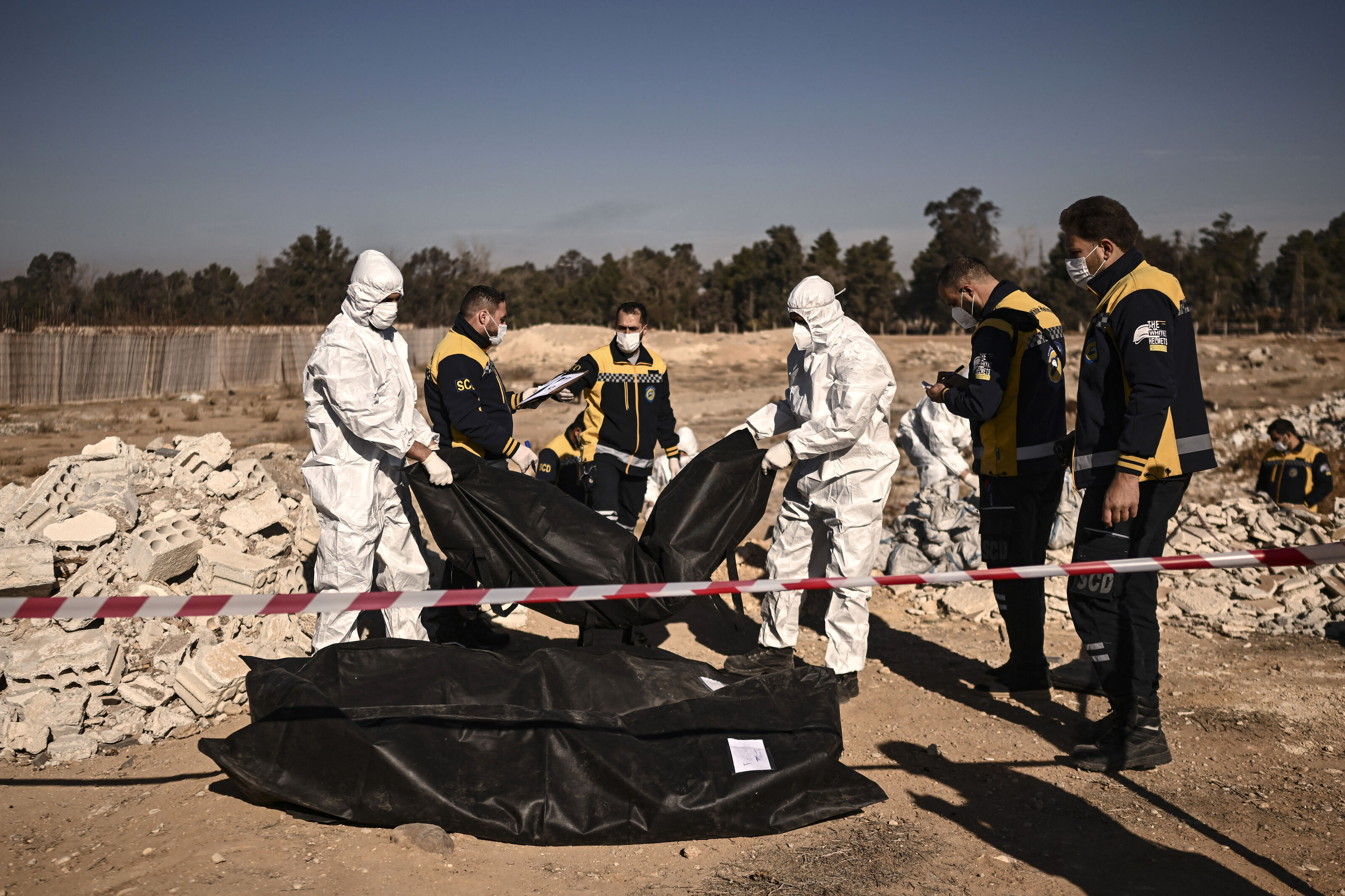 Members of Syria's White Helmets civil defence transport body-bags containing human remains that were recovered from a mass grave, in Damascus, on December 16, 2024. 