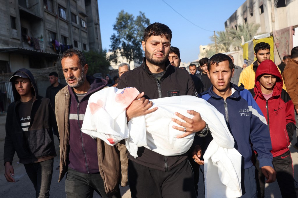 A relative carries the body of a child, one of four members of the Palestinian al-Qadra family killed in an Israeli strike that hit their tent north of Khan Younis in Gaza on January 18, 2025. (Bashar Taleb/AFP)