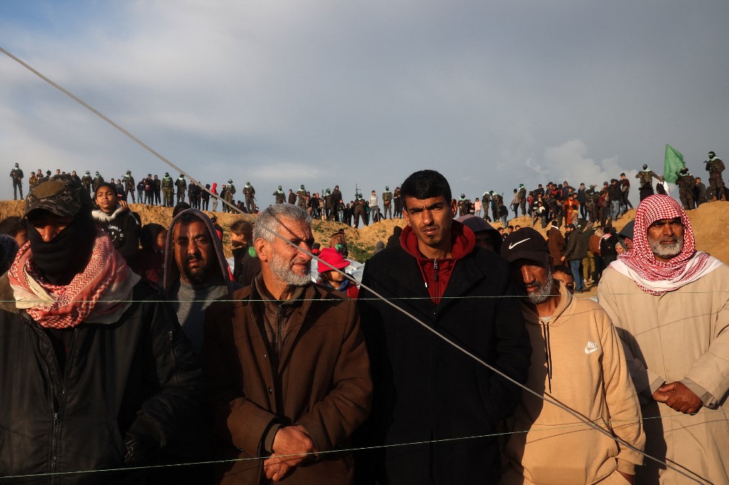 Palestinians gather as Hamas fighters stand at attention ahead of the handing over the bodies of four Israeli captives in Khan Yunis in the southern Gaza on February 20, 2025. (AFP/Eyad Baba)