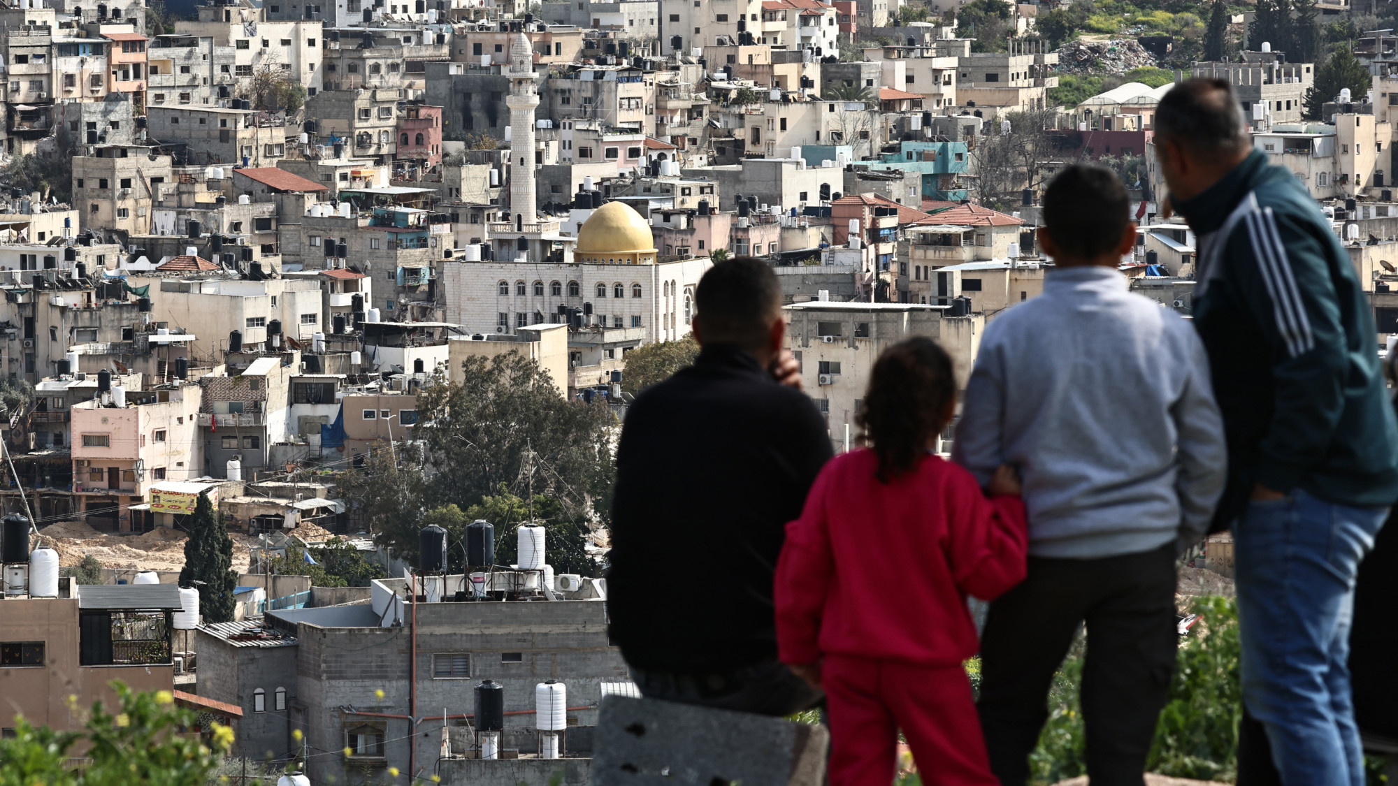 People forced out of the Nur Shams camp for Palestinian refugees watch the Israeli assault from a nearby hill, amid an ongoing offensive in the occupied West Bank, on 6 March 2025 (AFP/Zain Jaafar)