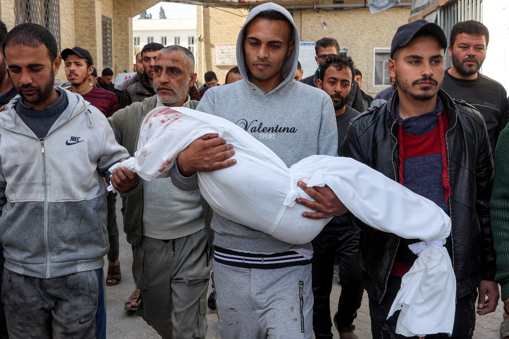 A man carries the wrapped body of a victim who was killed in overnight Israeli strikes on Gaza City, during a funeral at the Al-Ahli Arab Hospital in Gaza City on 25 March 2025 (AFP)