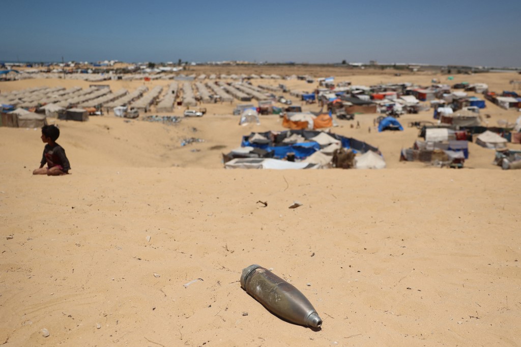 An unexploded shell lies on a sand dune as a young boy sits near a makeshift camp for displaced Palestinians in the area of Tel al-Sultan in Rafah in the southern Gaza Strip on May 30, 2024. (AFP)
