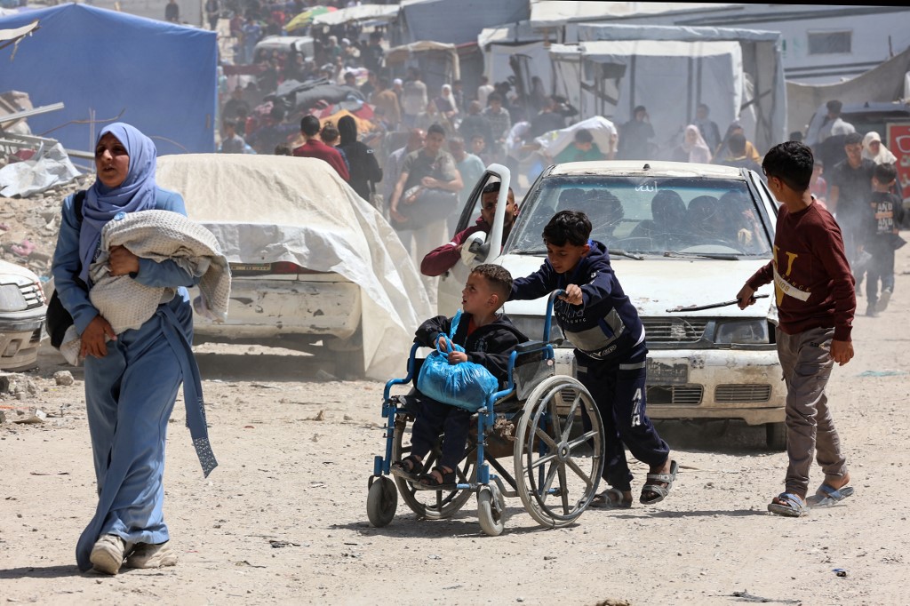 A woman carrying a baby walks ahead of a child pushing another in a wheelchair, as Palestinians flee Gaza City's eastern neighbourhood of Shujaiya following a forced evacuation order issued by the Israeli military on 3 April, 2025.