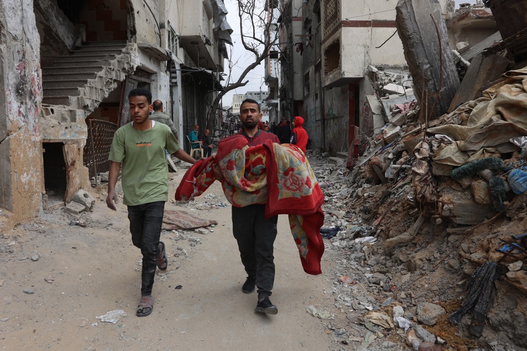 A Palestinian man carries the body of a victim of an Israeli strike on a residential area in Gaza City's Shujaiyya neighbourhood, on 9 April, 2025. (AFP)