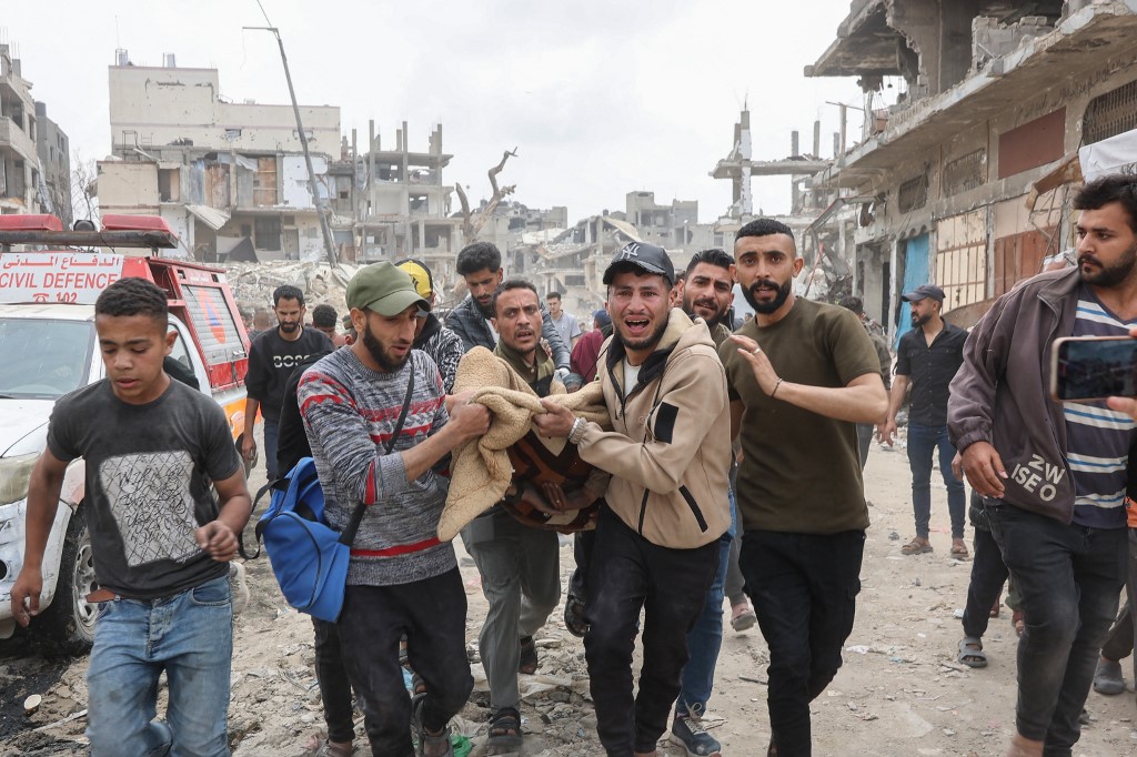 Palestinian men rush carrying in a blanket a victim of an Israeli strike on a residential area in Gaza City's Shujaiyya neighbourhood, on April 9, 2025. 