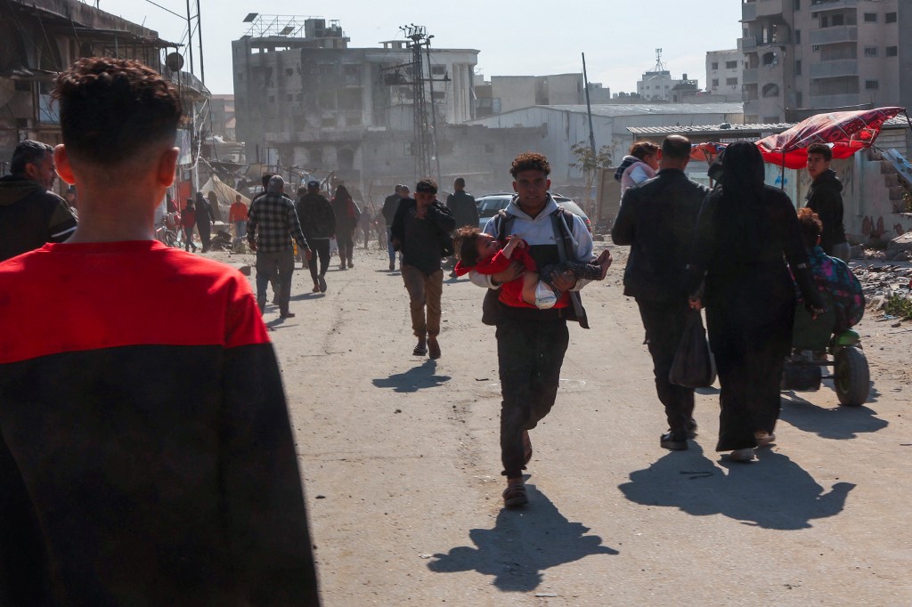 A Palestinian man rushes off carrying an injured girl following an Israeli strike on a metalsmith workshop at the Zaytoun neighbouhood in Gaza City on April 13, 2025. (AFP)
