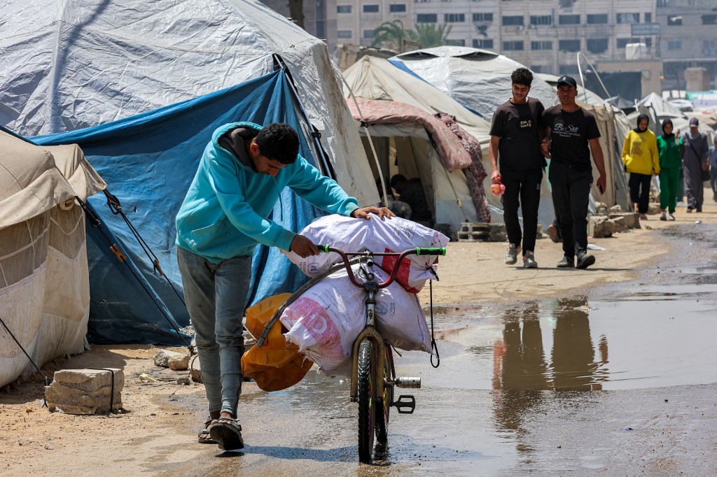 A boy pushes a bicycle loaded with sacks of food aid past tents in Gaza City on April 21, 2025. (AFP)