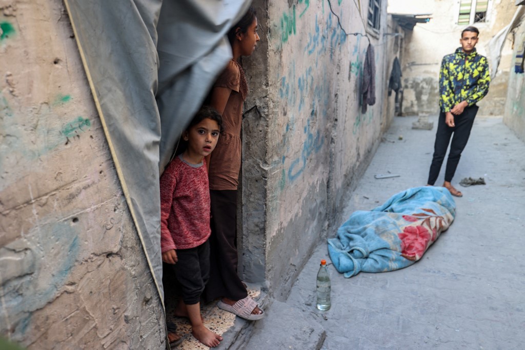 People stand over the shrouded body of a person killed in an Israeli strike that hit a building in the Bureij camp for Palestinian refugees in the central Gaza Strip on May 2, 2025.
