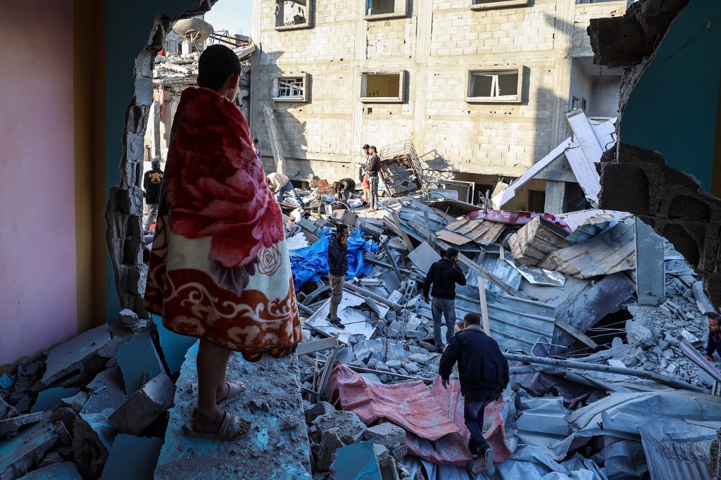 A youth draped in a blanket looks on as people look for survivors in the rubble of a building hit in an Israeli strike in the Bureij camp for Palestinian refugees in the central Gaza Strip on May 2, 2025.