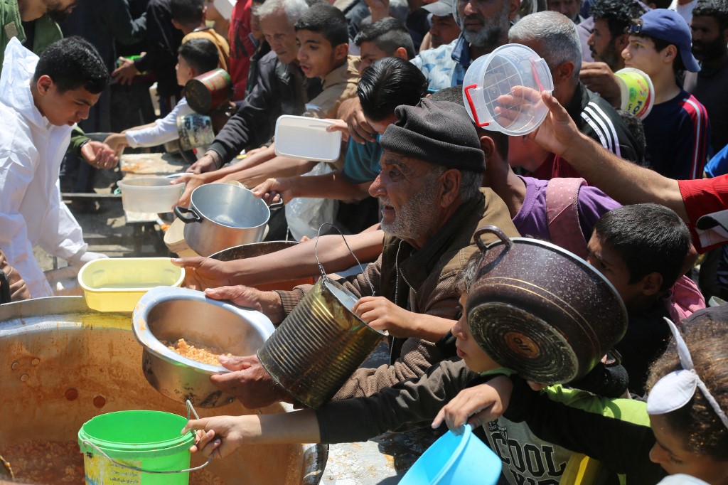 Palestinians queue for hot food portions distributed by a charity kitchen at the Nuseirat refugee camp in the central Gaza Strip on May 5, 2025. 