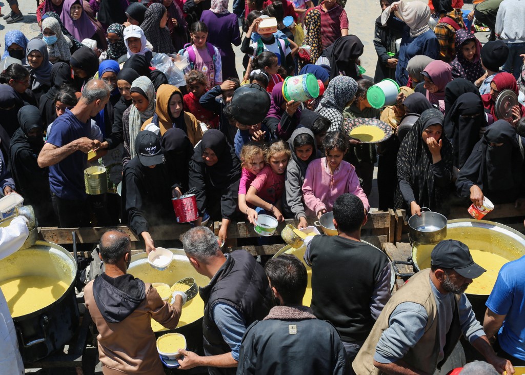 Displaced Palestinians queue for a portion of hot food at a charity kitchen at the Nuseirat refugee camp in the central Gaza Strip on May 5, 2025. (AFP)