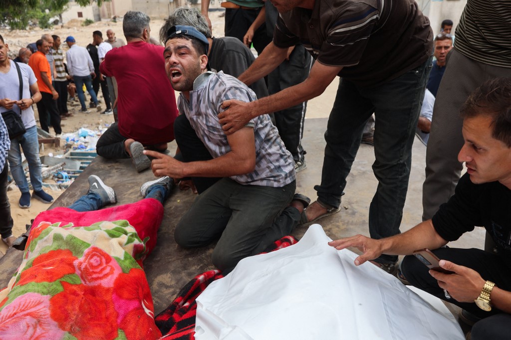 A Palestinian man mourns as others transport bodies of people killed in Israeli strikes on Jabalia a day earlier, at Al-Shifa hospital in Gaza City on June 23, 2025.