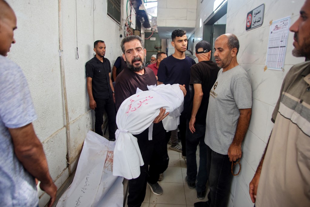 A Palestinian mortuary worker carries the body of a child at Al-Shifa hospital in Gaza City, on 26 June, 2025, (Reuters)