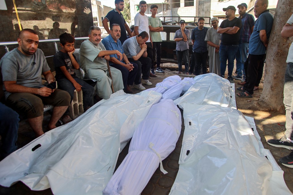 Palestinian mourners sit near the bodies of people killed during overnight Israeli strikes, at Al-Shifa hospital in Gaza City on June 26, 2025,