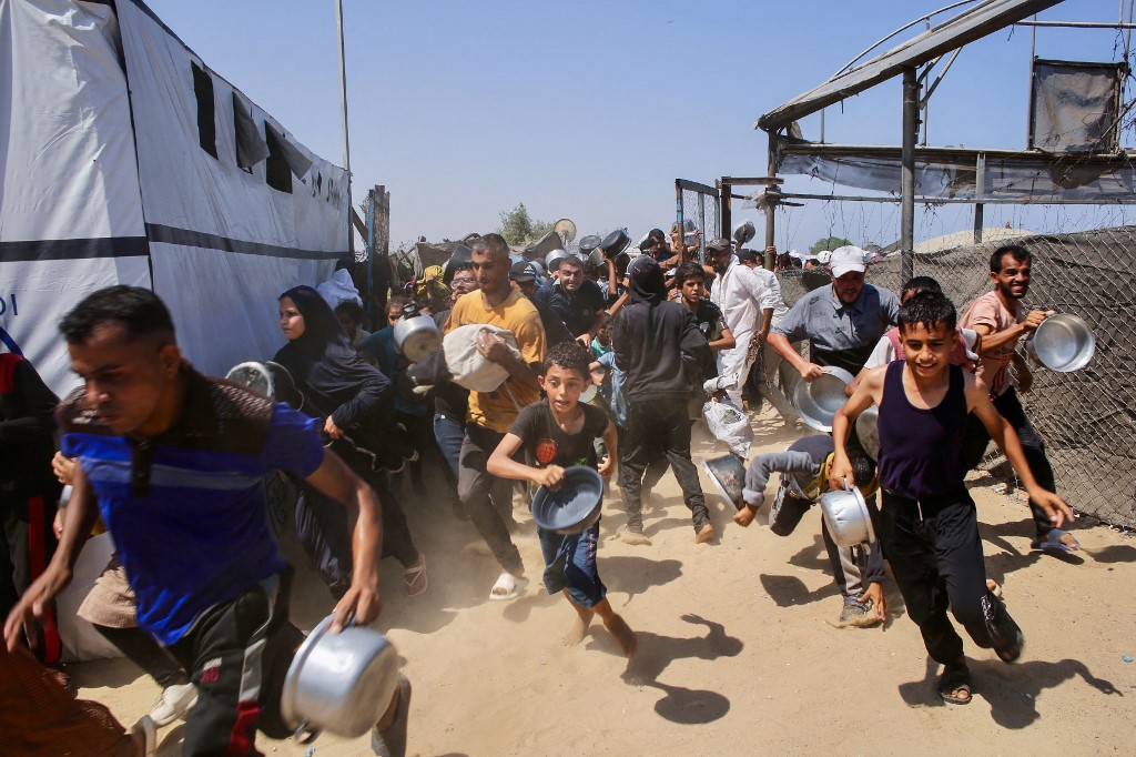 Palestinians rush to queue in line at a charity kitchen in the Mawasi area of Khan Younis in the southern Gaza Strip on July 22, 2025. AFP