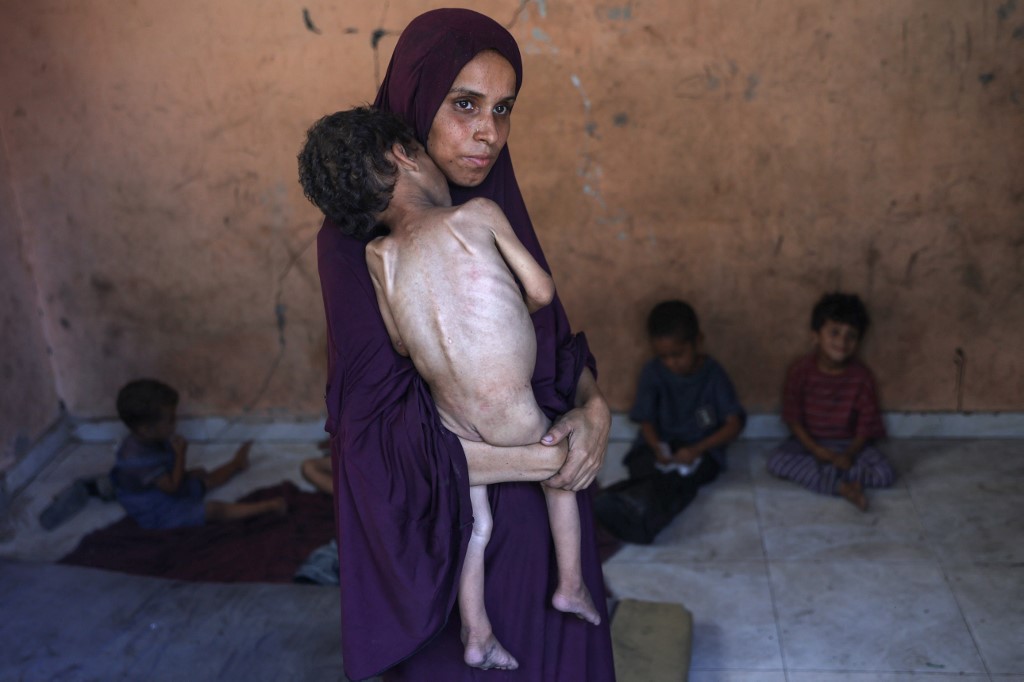 Naeema, a 30-year-old Palestinian mother, carries her malnourished 2-year-old son Yazan as they stand in their damaged home in the Al-Shati refugee camp, west of Gaza City, on July 23, 2025.