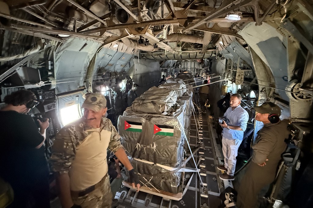 A videographer films next to airmen by a shipment of humanitarian aid packages loaded onto a C-130 Hercules military transport aircraft during an airdrop mission over the Gaza Strip on July 30, 2025.