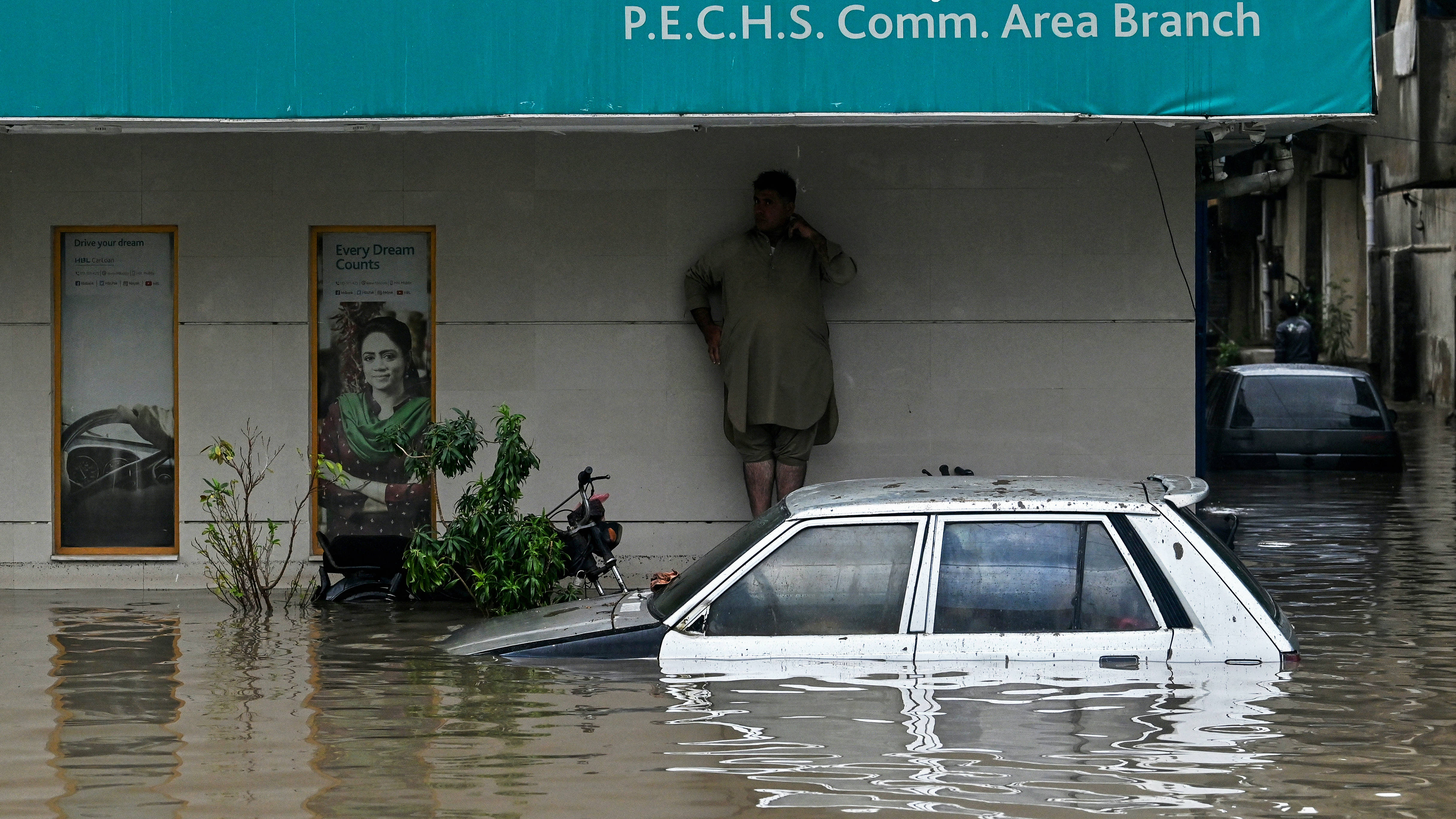 A man takes shelter as a car lies partially submerged in floodwaters along a street after heavy rainfall in Karachi on 19 August (Asif HASSAN / AFP)