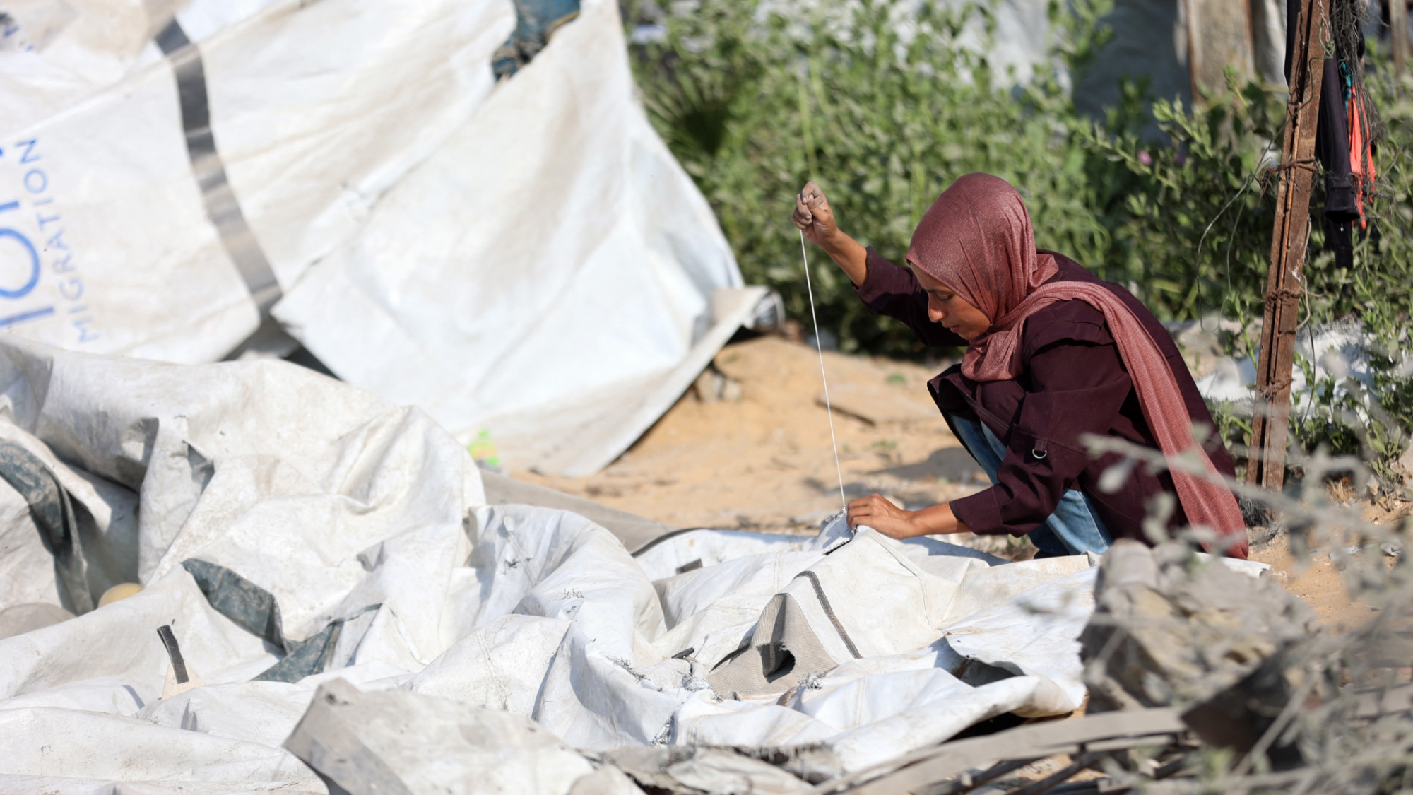 A Palestinian woman mends a torn up tent, after an Israeli strike levelled a building and damaged surrounding temporary shelters in Gaza City on 13 September 2025 (AFP/Omar al-Qattaa)