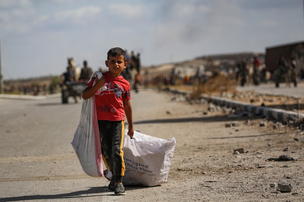 A Palestinian boy carries a bag and drags another behind him as he returns from a food distribution point run by the US and Israeli-backed Gaza Humanitarian Foundation (GHF) group, near the Netsarim corridor in the central Gaza Strip on October 5, 2025. 