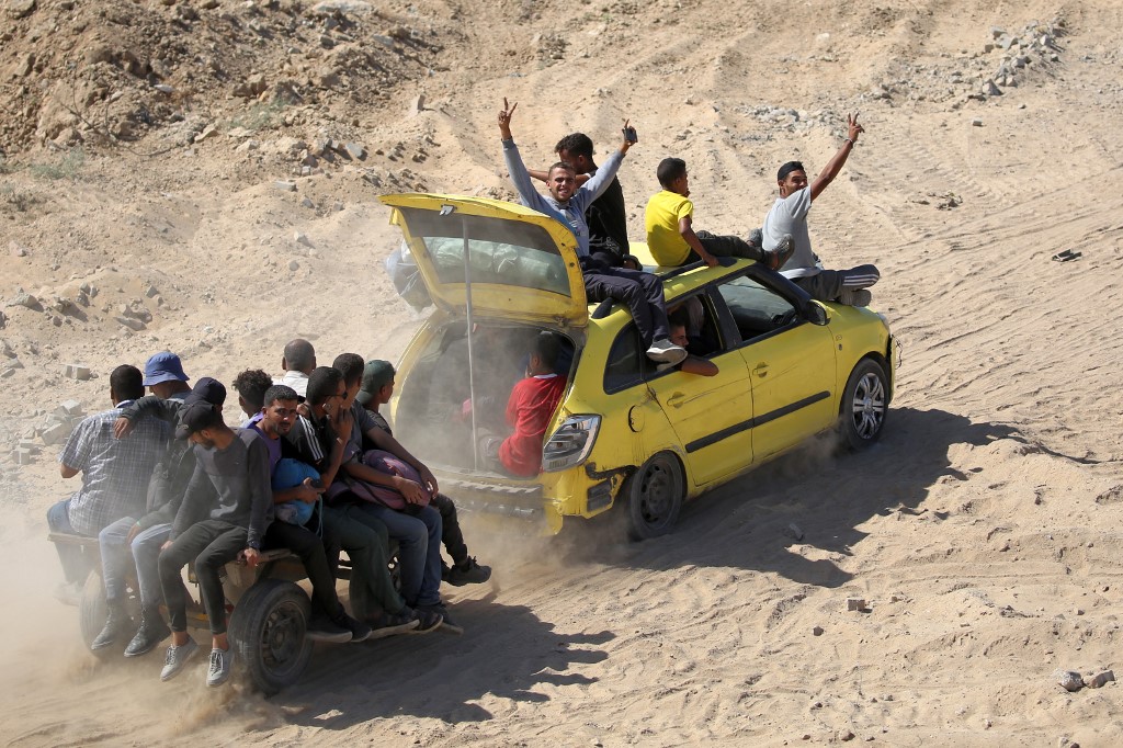 Men gesture as they sit atop a vehicle towing another cart with passengers aboard moving along a dirt road to Gaza City near Nuseirat in the central Gaza Strip on October 10, 2025. 