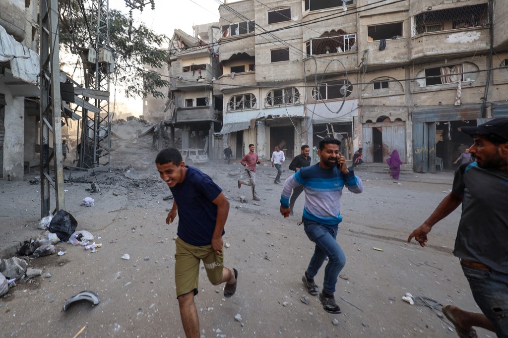 People run for cover following an Israeli strike that targeted a building in the Bureij camp for Palestinian refugees in the central Gaza Strip on October 19, 2025. 
