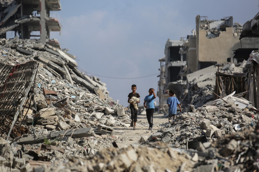 Palestinian boys make their way through the rubble of destroyed buildings in the Al-Shatee refugee camp, east of Gaza City, on November 8, 2025.