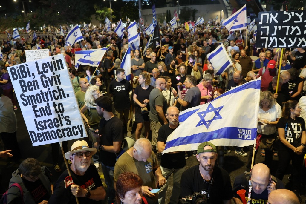 Israeli anti-government protesters lift placards and flags during a demonstration against Prime Minister Benjamin Netanyahu and demand the establishment of a state commission of inquiry into the events of 7 October, in Tel Aviv on 8 November, 2025. (AFP)