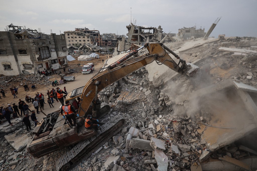 Civil Defence personnel use an excavator to search for the remains of victims in the rubble of a destroyed building in the Bureij refugee camp, in the central Gaza Strip, on 6 December, 2025. (AFP)