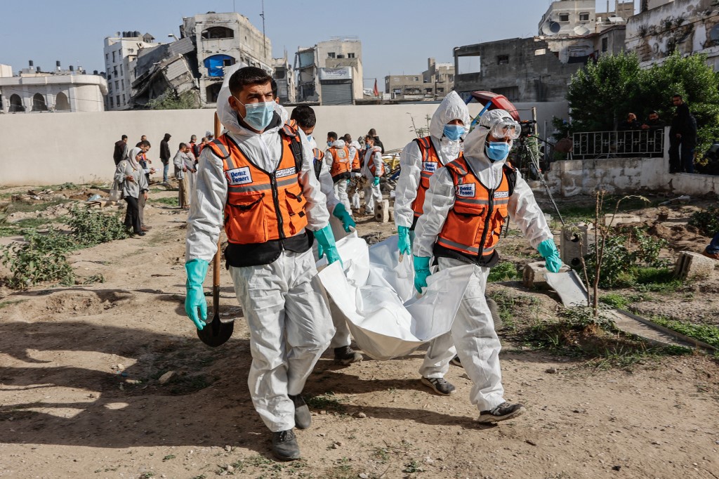 Civil defence personnel carry a body bag containing human remains after exhuming graves inside the Al-Ahli Arab Baptist Hospital to transfer the remains to official burial sites in Gaza City on December 7, 2025. 